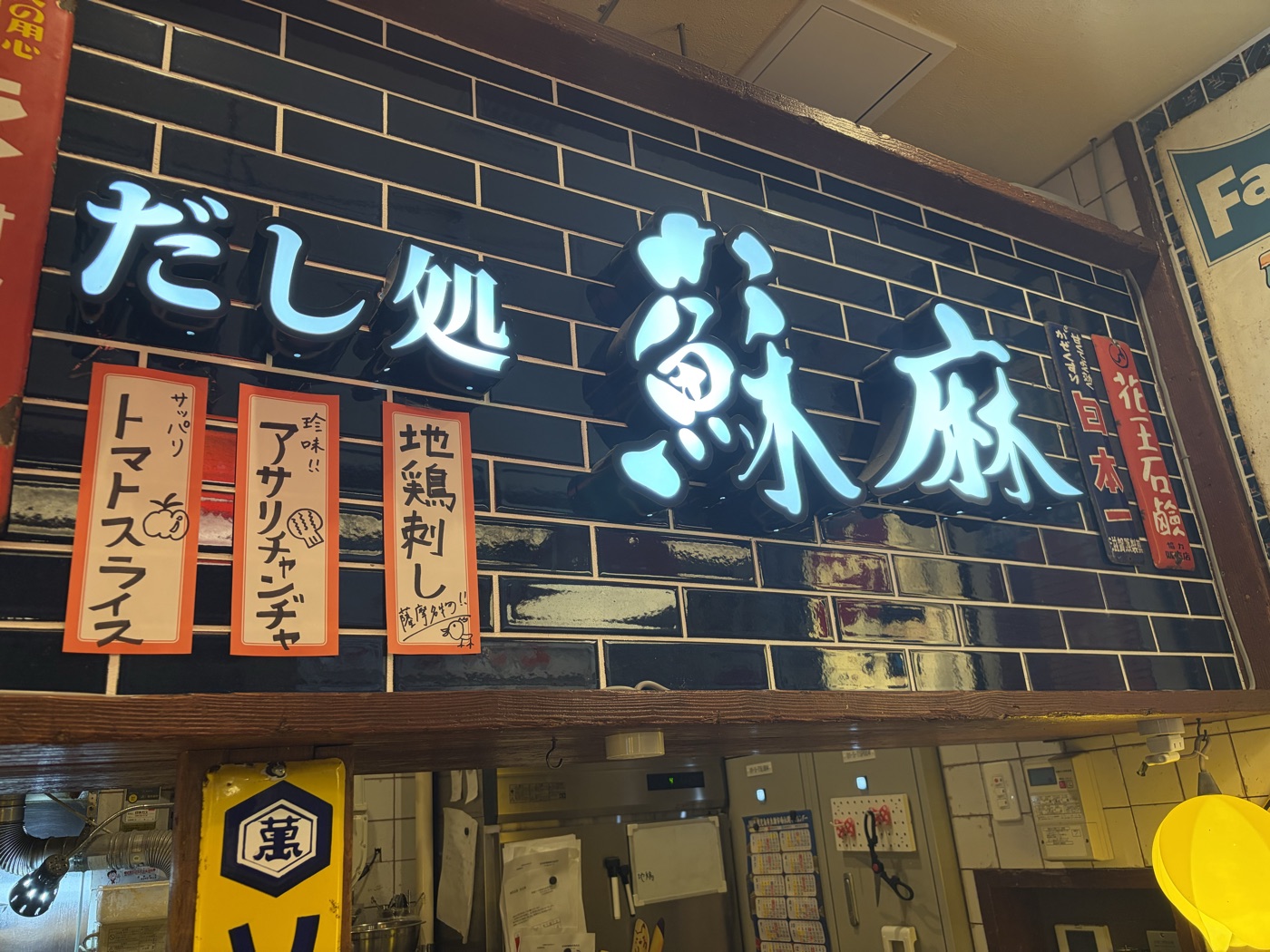 だし処 蘇麻の看板。黒いタイル壁に青く光る「だし処 蘇麻」の文字